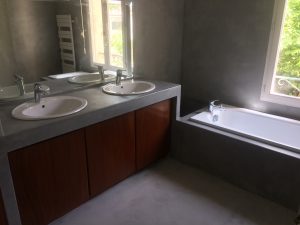 La salle de Bains qui fait la belle part au Béton Ciré avec des touches de bois précieux